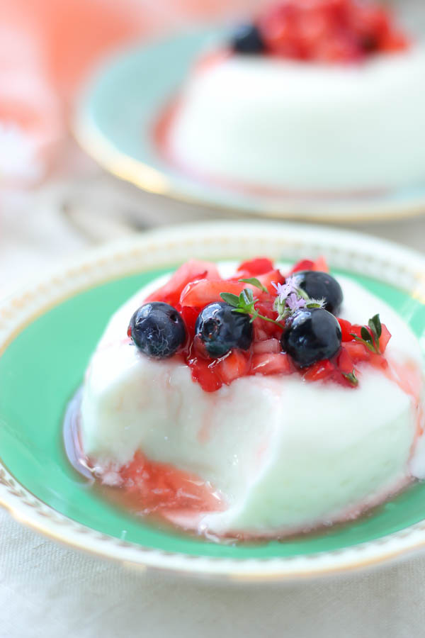 Italian panna cotta topped with macerated berries on a green saucer 