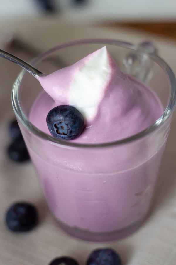 a spoon digging into a small glass with blueberry cheesecake mousse