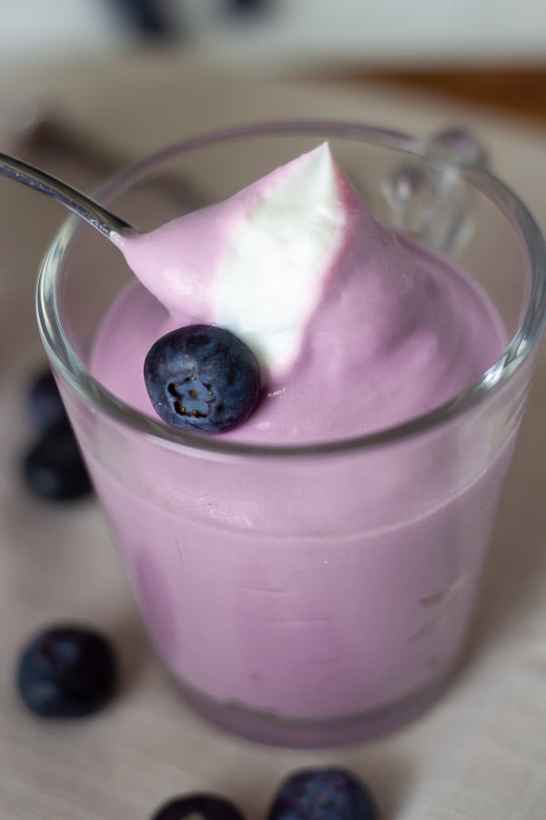 ein Löffel wird in ein veganes Blaubeer Käsekuchen Dessert im Glas getaucht