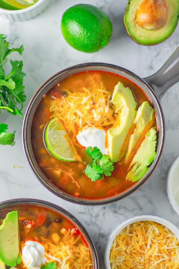 a bowl of Mexican chicken tortilla soup topped with cheese, avocado and sour cream