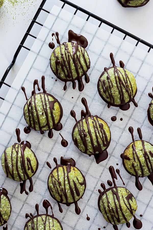 pistachio macaroons on a cooling rack being drizzled with dark chocolate 