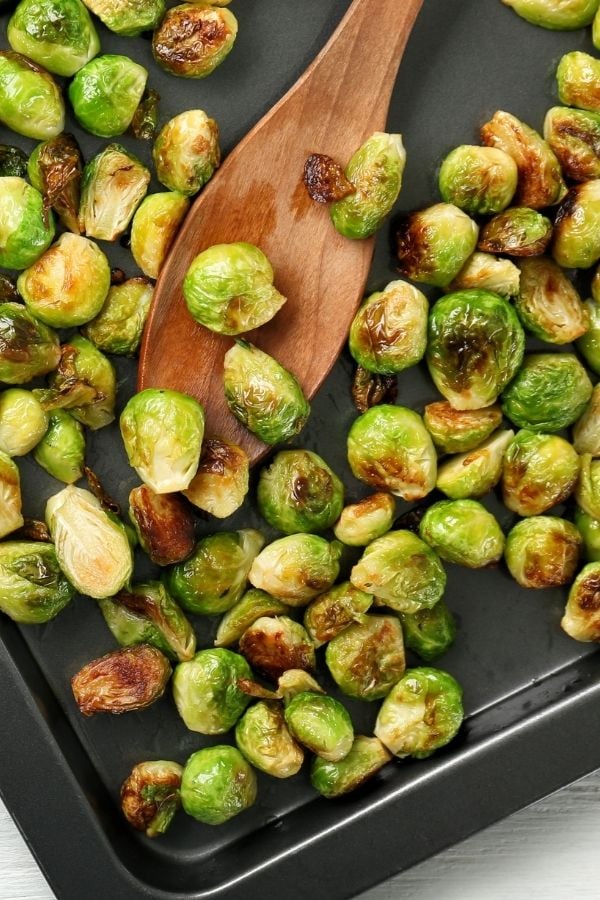 overhead shot of roasted brussel sprouts on a sheet pan with a wooden spoon 