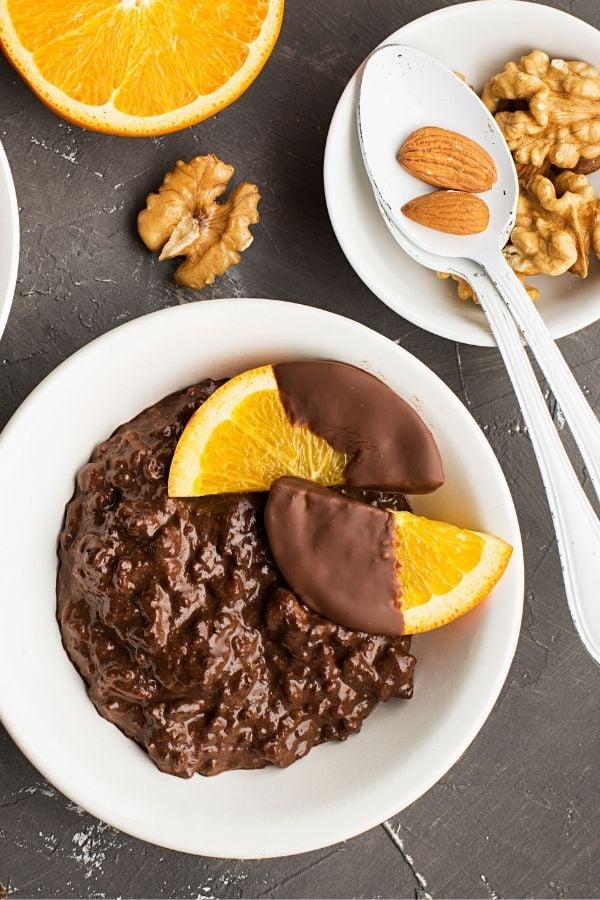 eine Schale veganes Schokoladen Porridge mit in Schokolade getauchten Orangenscheiben und Nüssen dekoriert