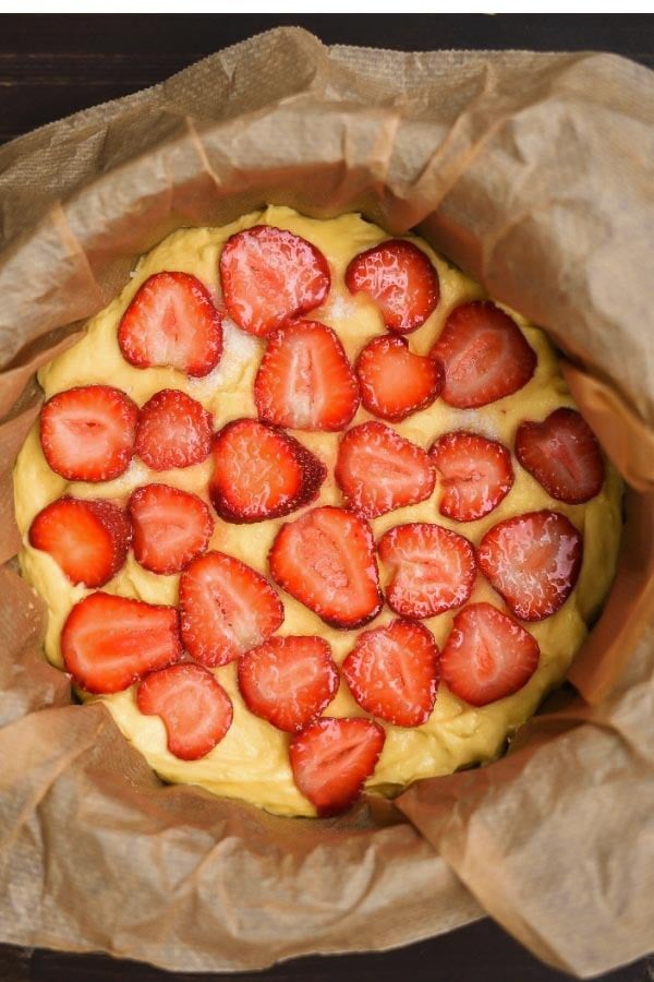 cake batter being topped with sliced strawberries to make fresh strawberry cake from scratch 
