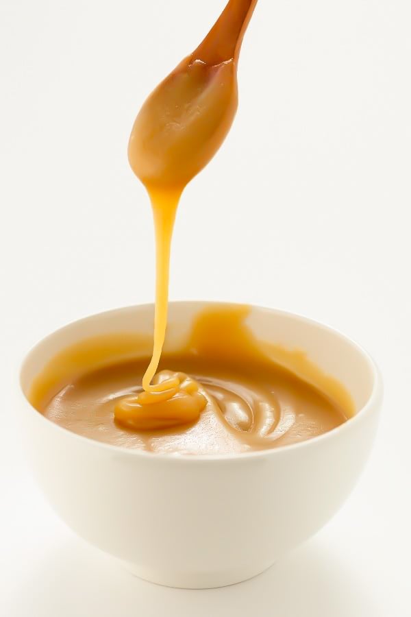 vegan tahini caramel sauce running off a spoon into a bowl 