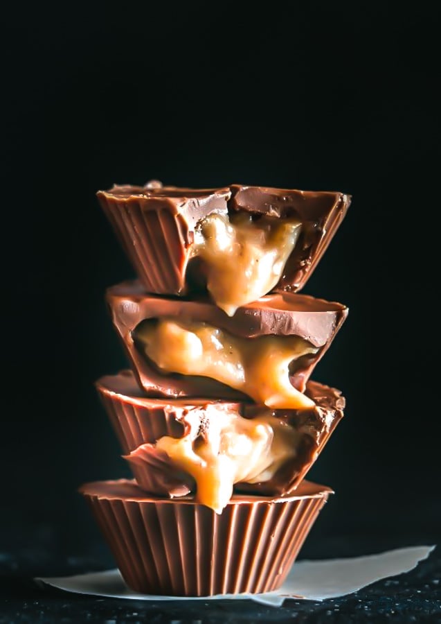 a stack of vegan salted tahini caramel chocolate cups against black background with tahini caramel oozing out the halved cups