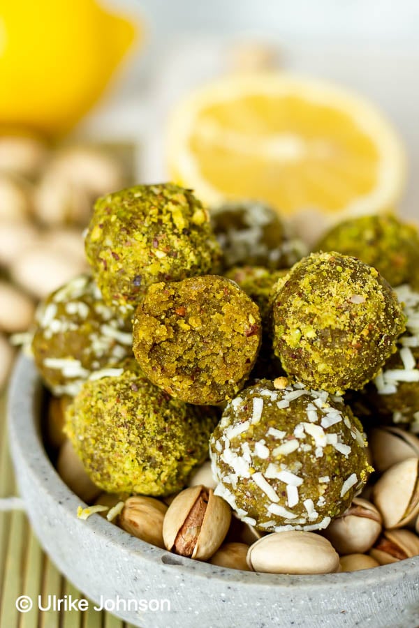 vegan glutenfree no bake pistachio energy balls stacked in a bowl, one with a bite taken