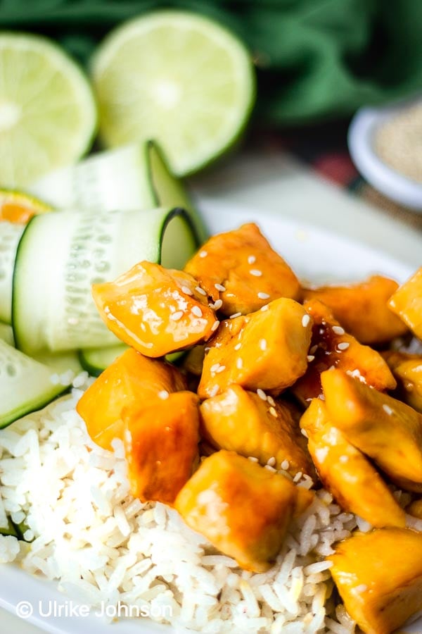 healthy Chinese Orange Chicken in sticky citrus sauce served on a platter with rice and cucumber salad