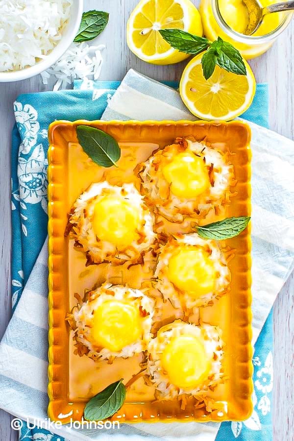coconut macaroons filled with lemon curd on a orange tray with lemons in the background