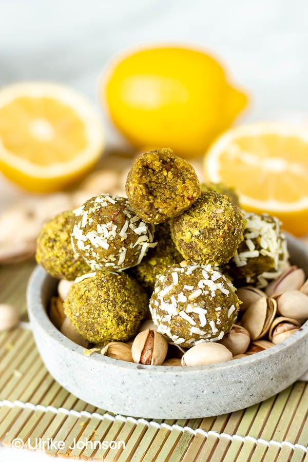healthy vegan lemon pistachio date energy balls in a small bowl with shelled pistachios and lemons on the side
