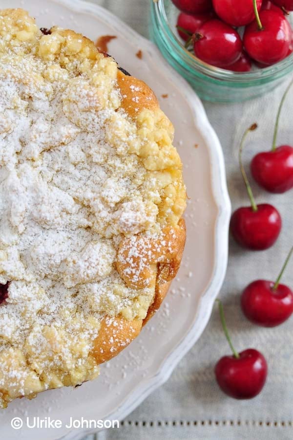 German apricot and cherry crumb cake on a cake plate with fresh cherries on the side