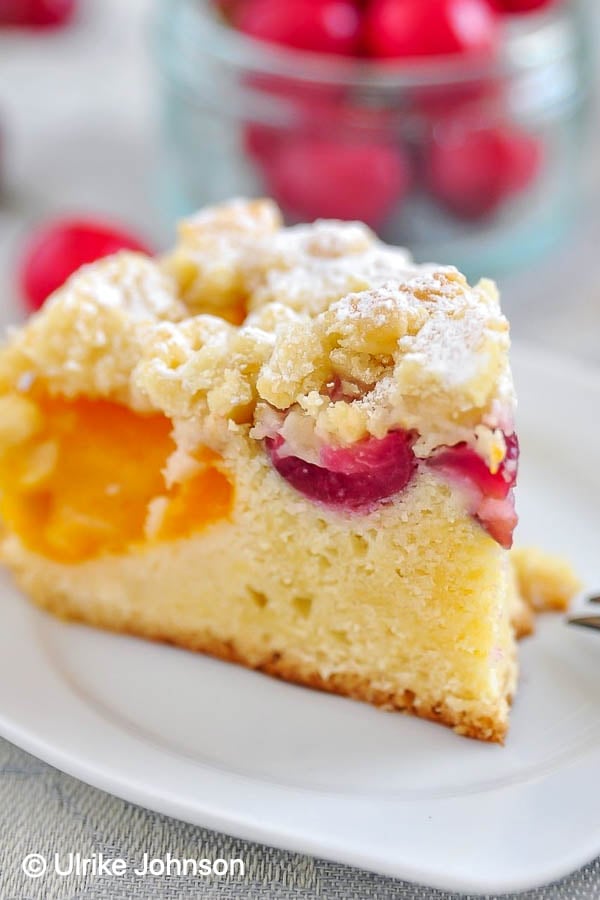 ein Stück saftiger Aprikosen Streuselkuchen mit Kirschen und Marzipanstreusel auf einem Kuchenteller