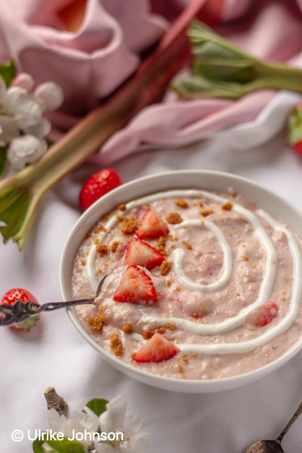eine Schale Rhabarber Erdbeer Porridge mit frischen Erdbeeren und Kekskrümeln dekoriert