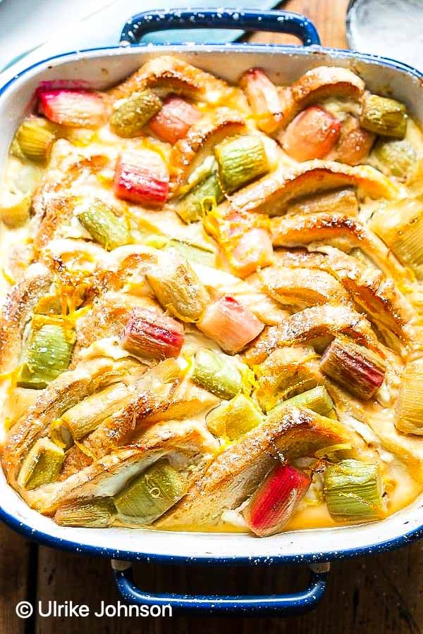 a casserole dish with homemade rhubarb bread pudding dusted with icing sugar and served with creme anglaise