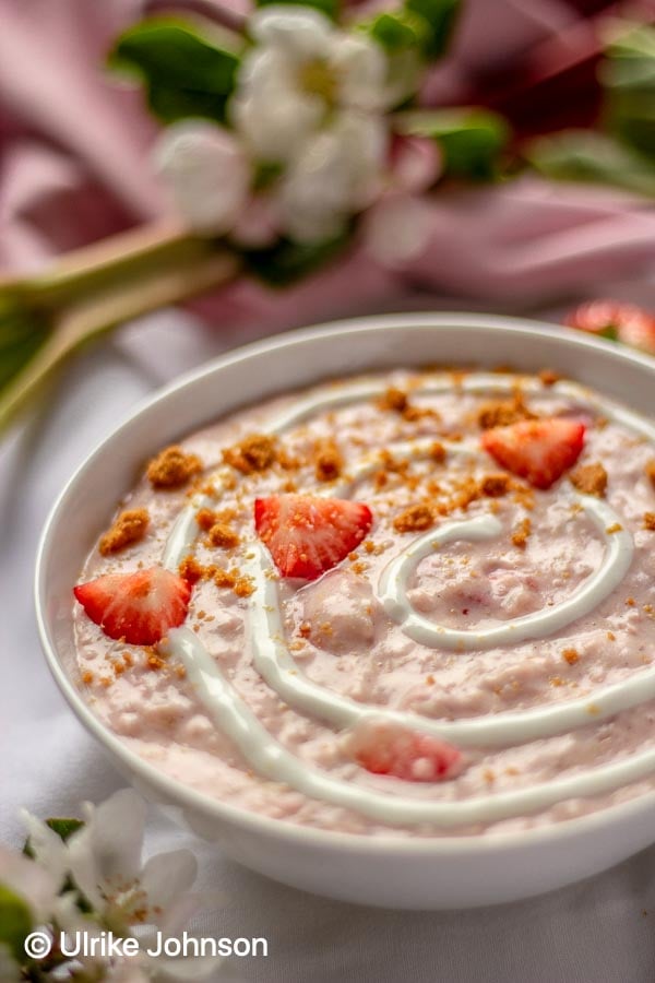 side view of strawberry rhubarb cheesecake porridge topped with fresh strawberries, yogurt and cookie crumbs 