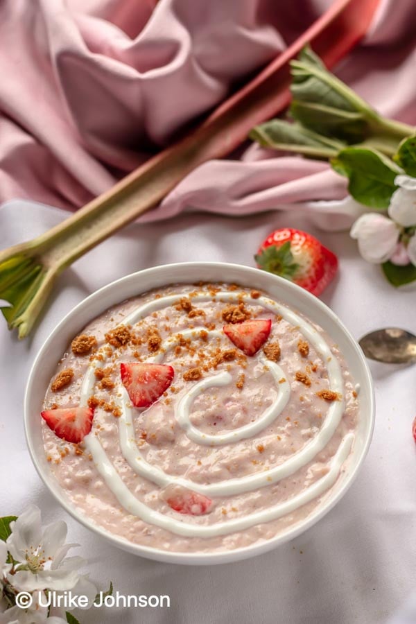 a strawberry rhubarb cheesecake oatmeal bowl decorated with cookie crumbs and fresh strawberries