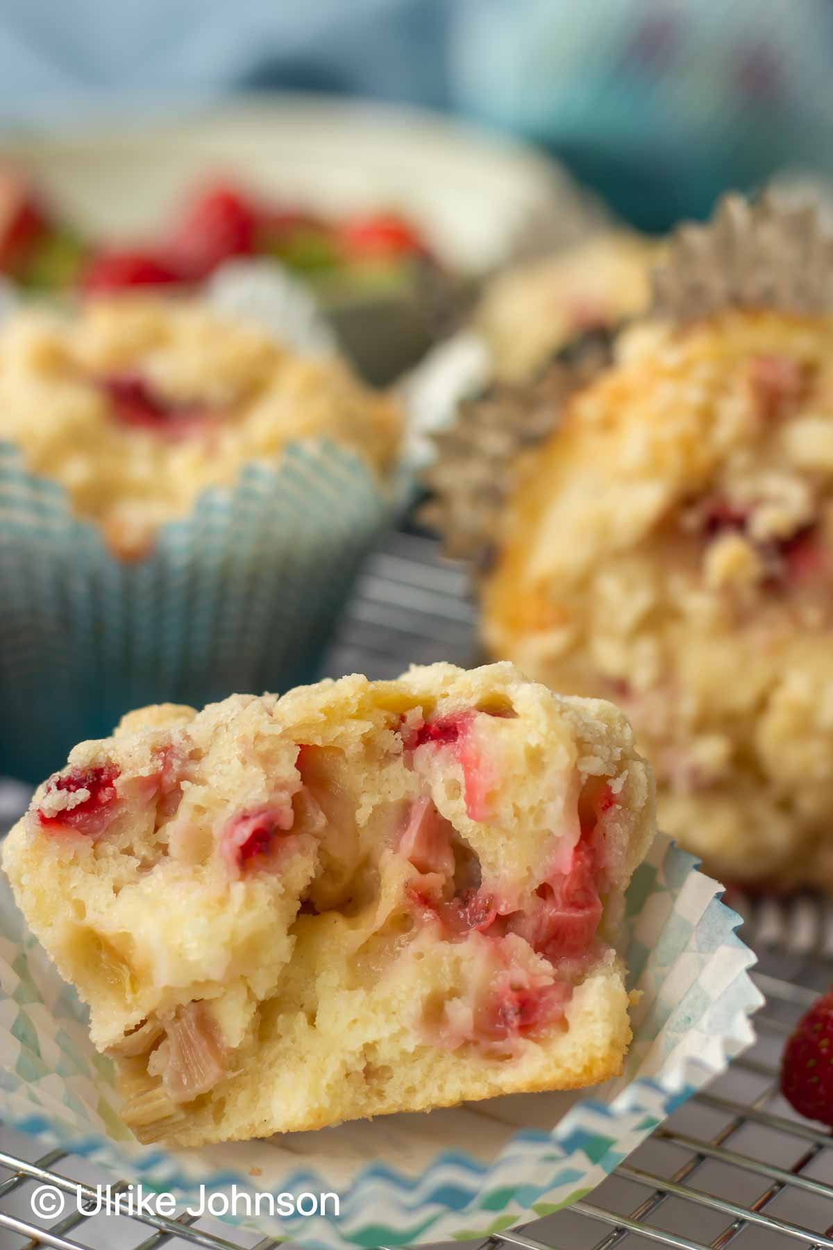 ein angebissener Erdbeer Rhabarber Muffin mit Streusel in einem Papierförmchen