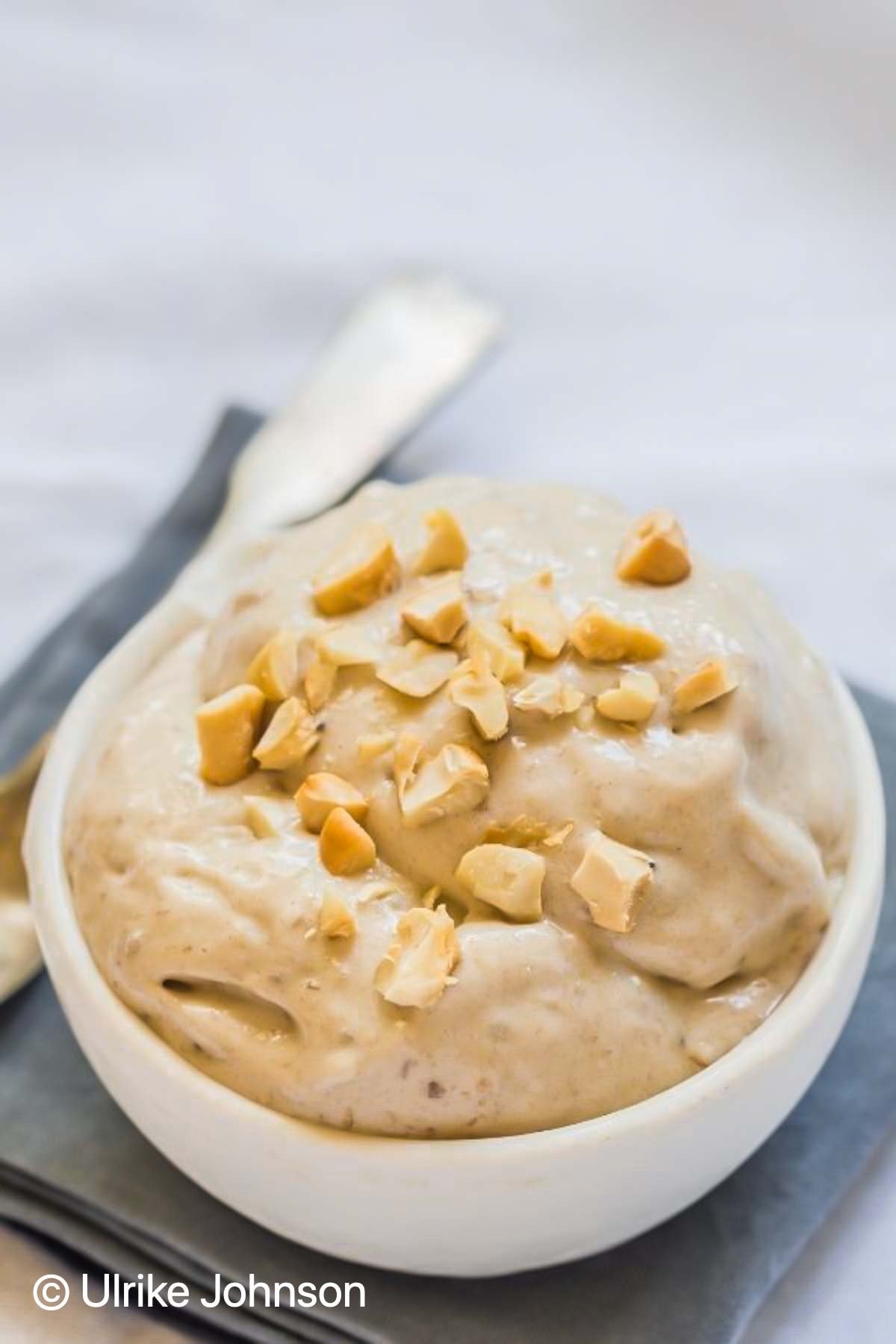a bowl of healthy vegan peanut butter nice cream topped with chopped roasted peanuts