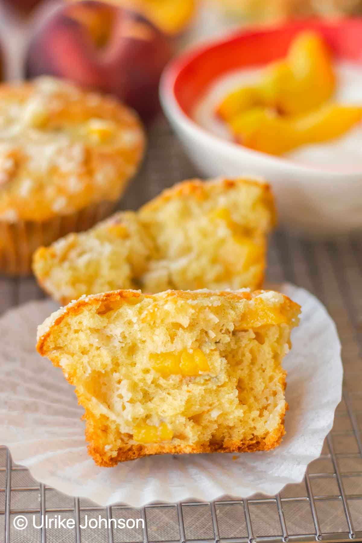 a halved peach muffin with chunks of fresh peached with a bowl of yogurt