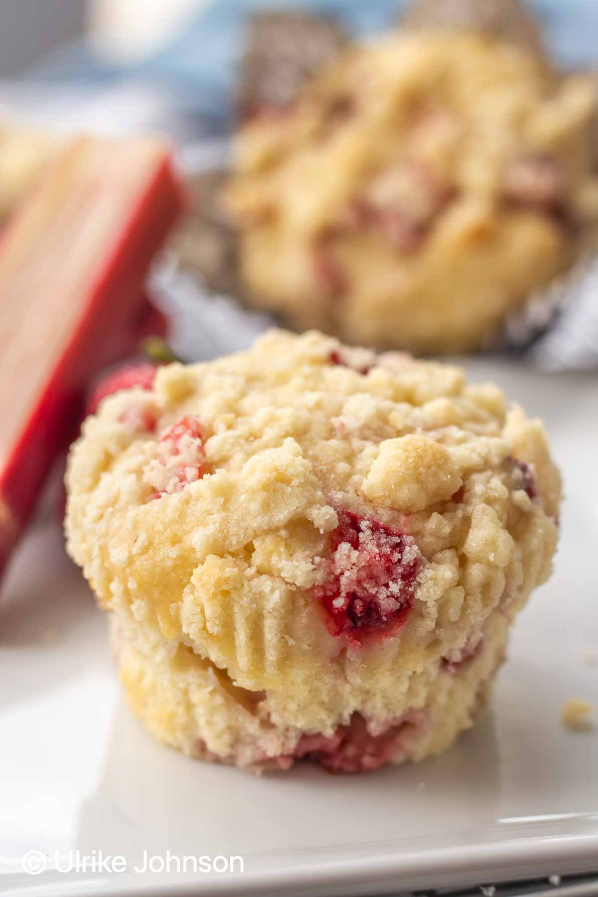 a Strawberry Rhubarb Streusel Muffin on a white paper plate with rhubarb stalks in the background
