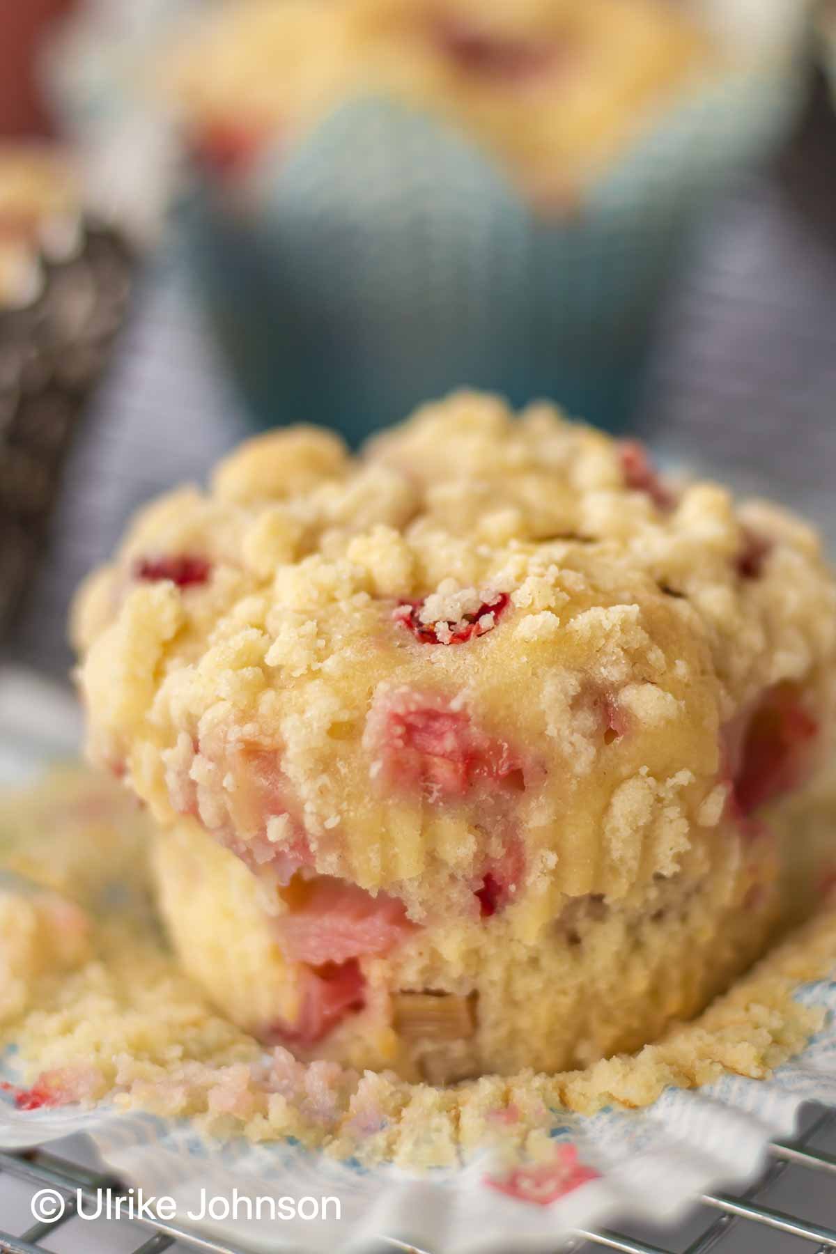 close up of a strawberry rhubarb crumble muffin with sour cream streusel topping being taken out of a paper liner