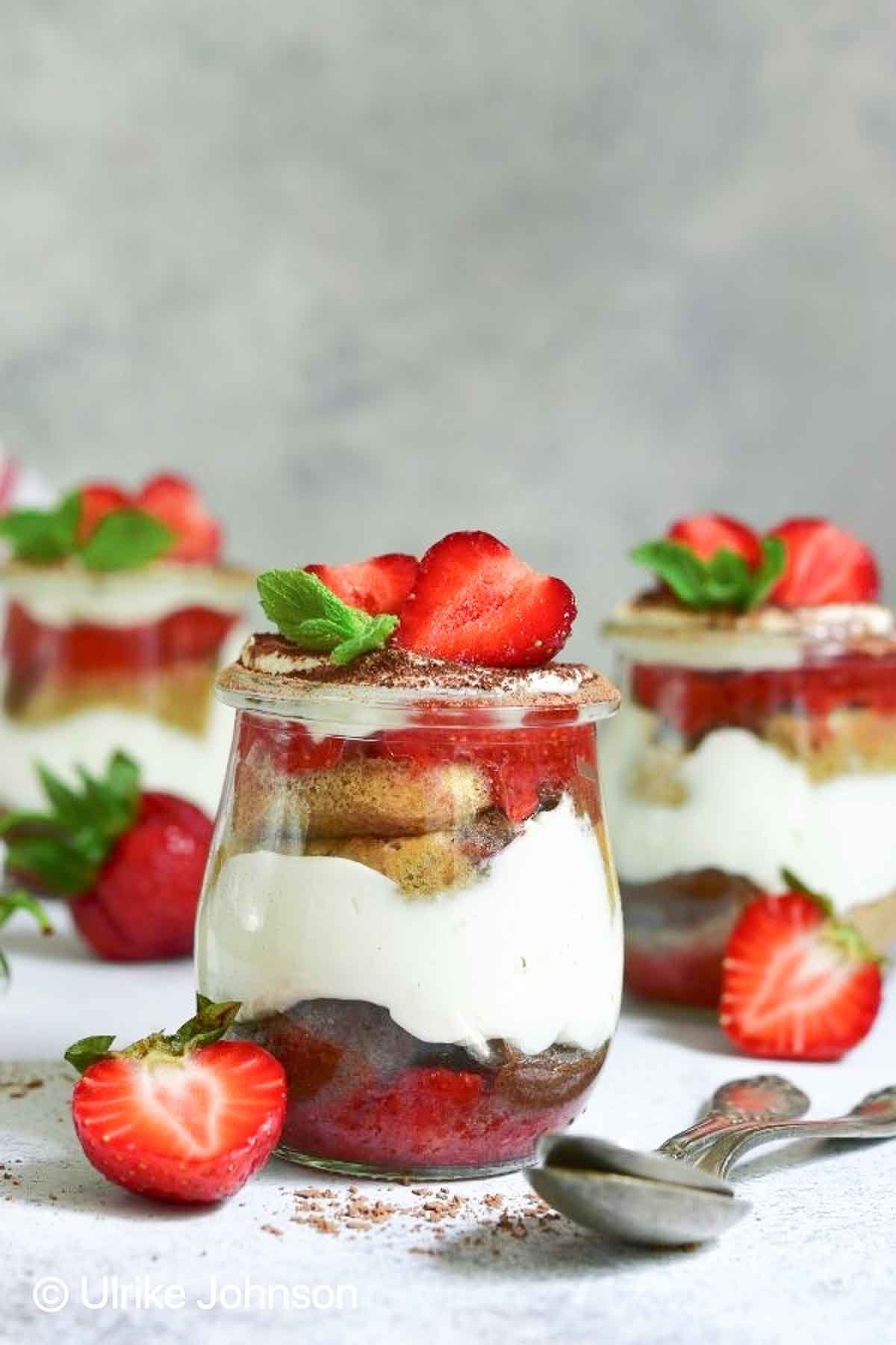 eggless strawberry tiramisu served in a dessert glass topped with cocoa powder fresh strawberries and mint