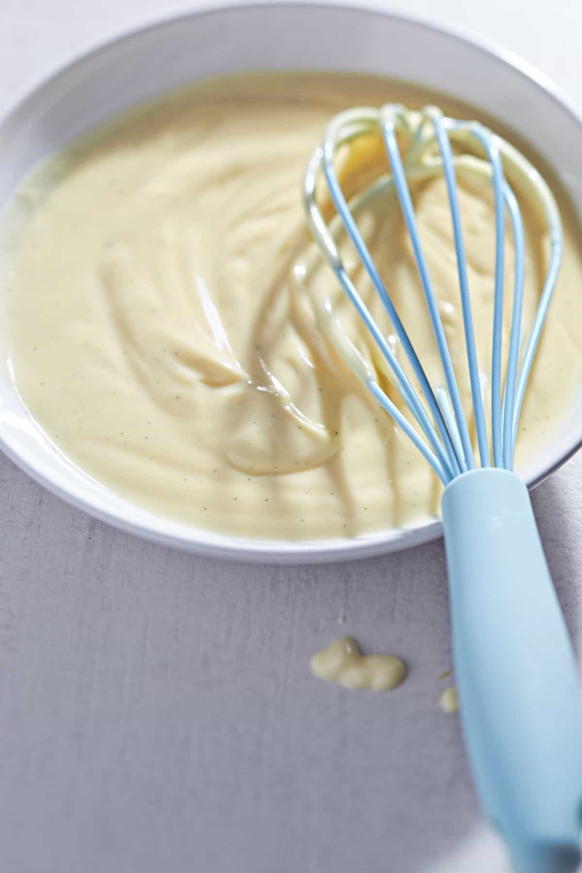 Vanillepudding mit echter Vanille in einer weißen Schale mit einem blauen Schneebesen