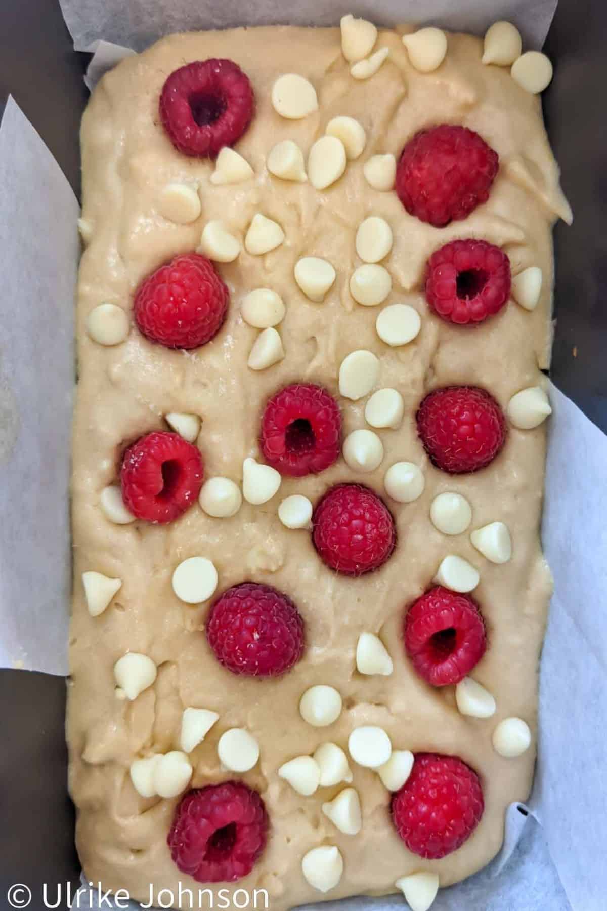 blondie batter being topped with white chocolate chips and fresh raspberries