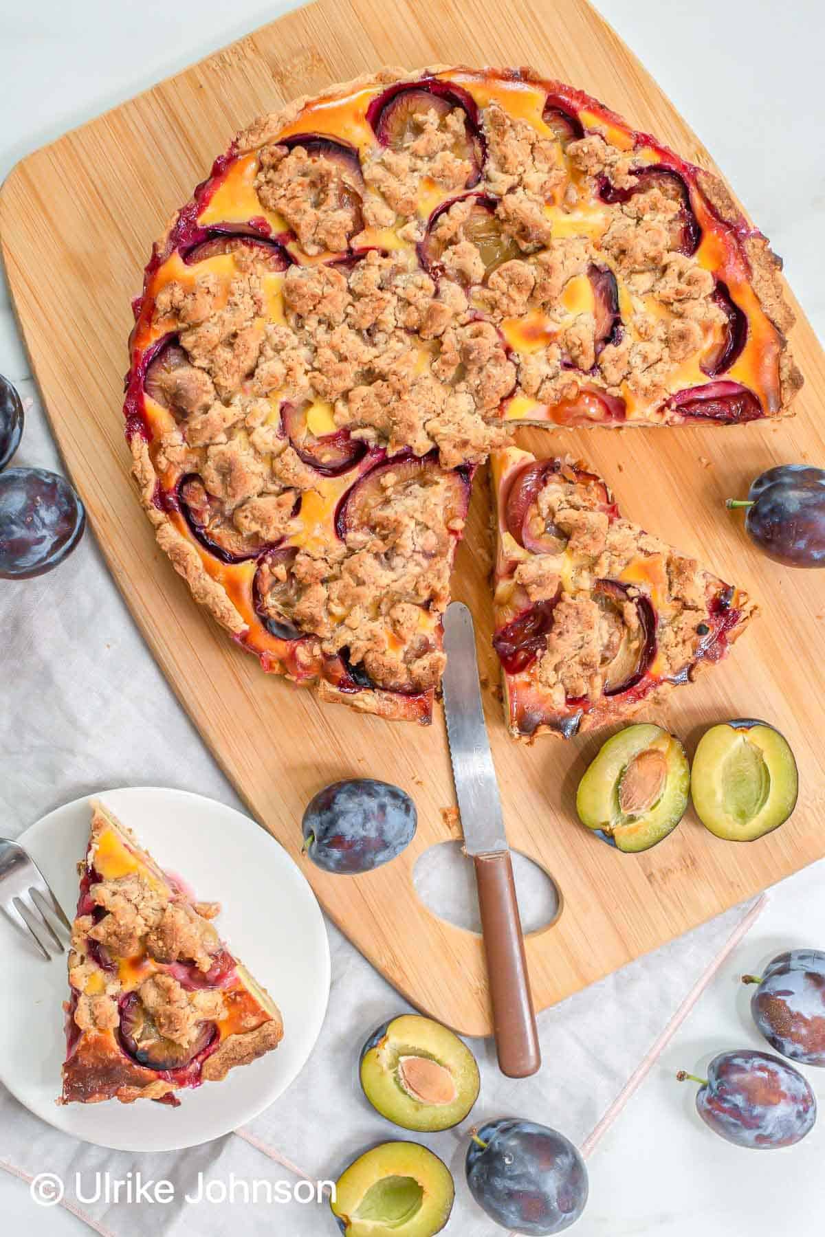 German plum custard tart with crumble topping being sliced on a wooden board 