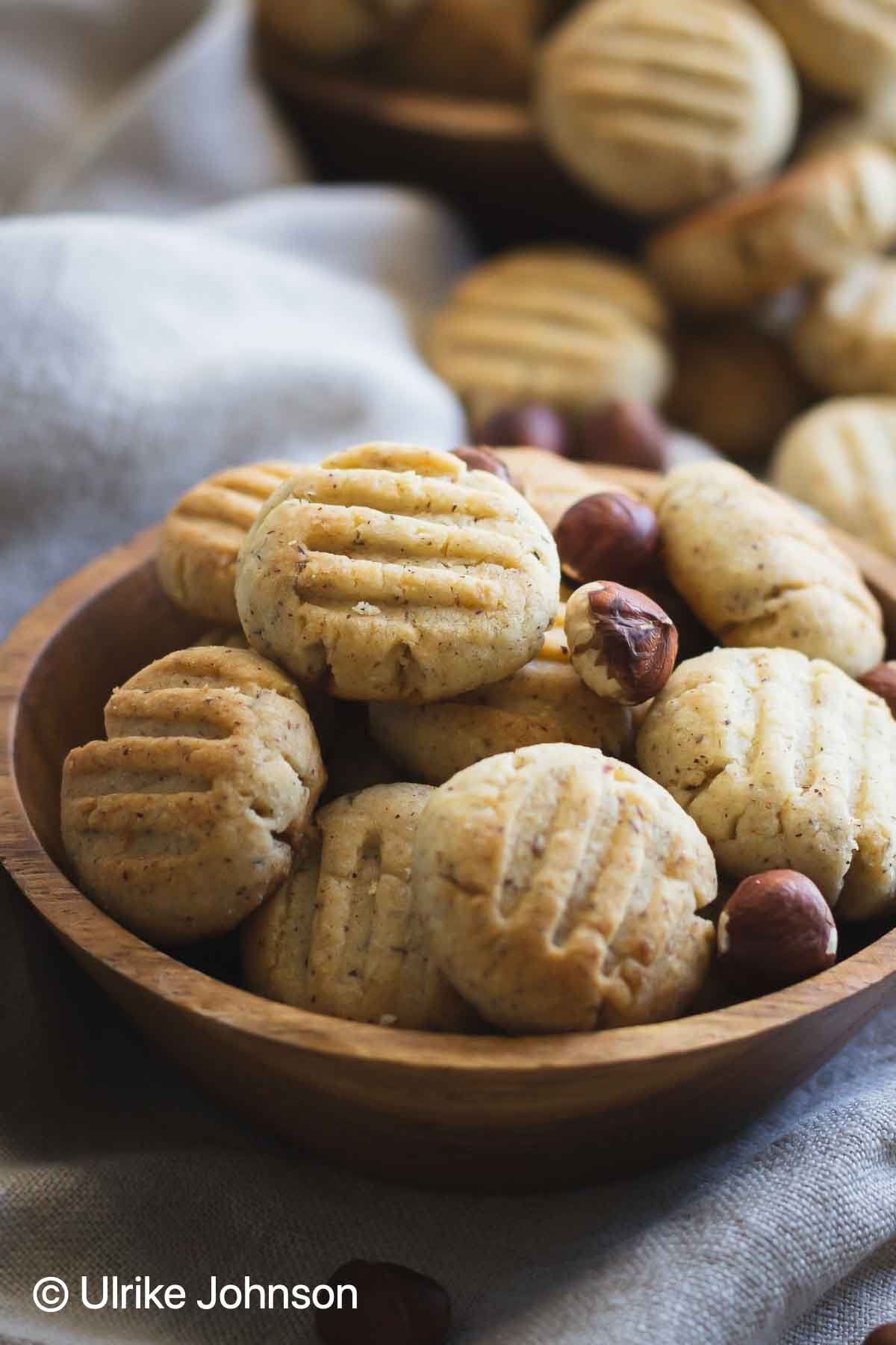 Soft German Hazelnut Cookies with whole hazelnuts in a wooden bowl