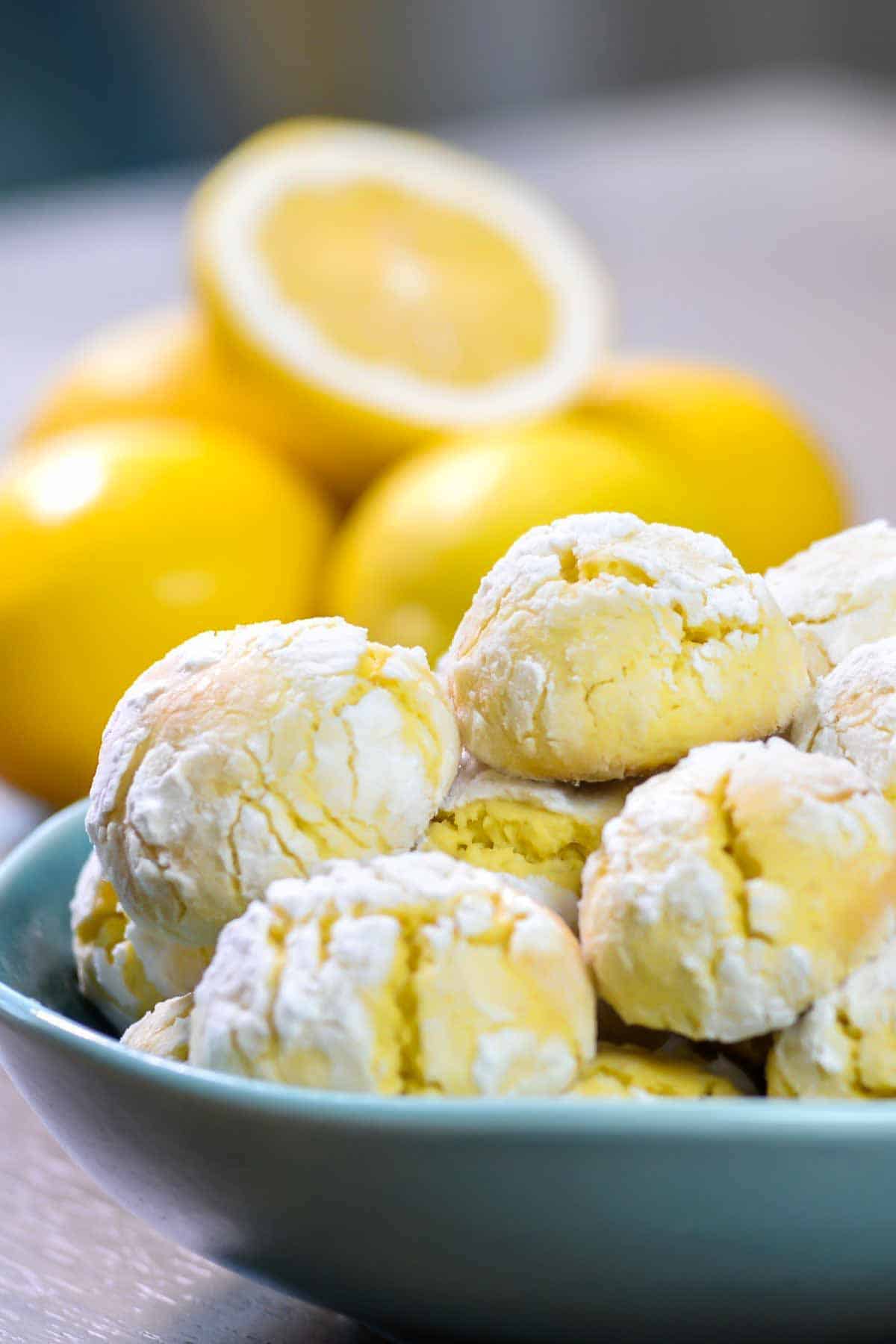 lemon amaretti cookies made with almond flour on a blue plate with fresh lemons in the background