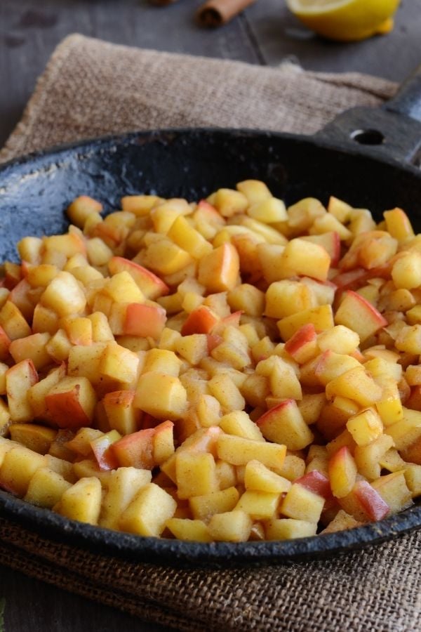 Apfelstücke in der Pfanne werden mit braunem Zucker und Bratapfel Punsch zu Kompott gekocht