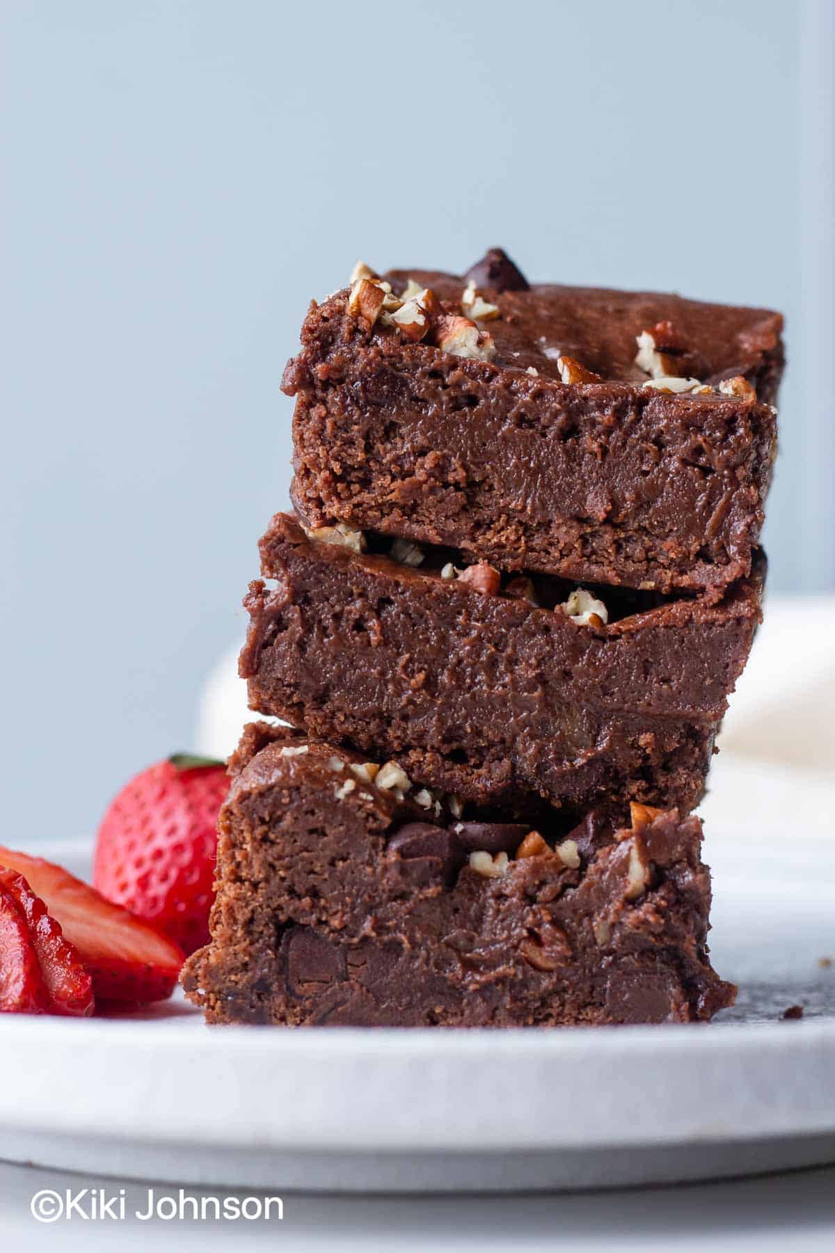 eggless Nutella Brownies stacked on a plate with strawberries on the side