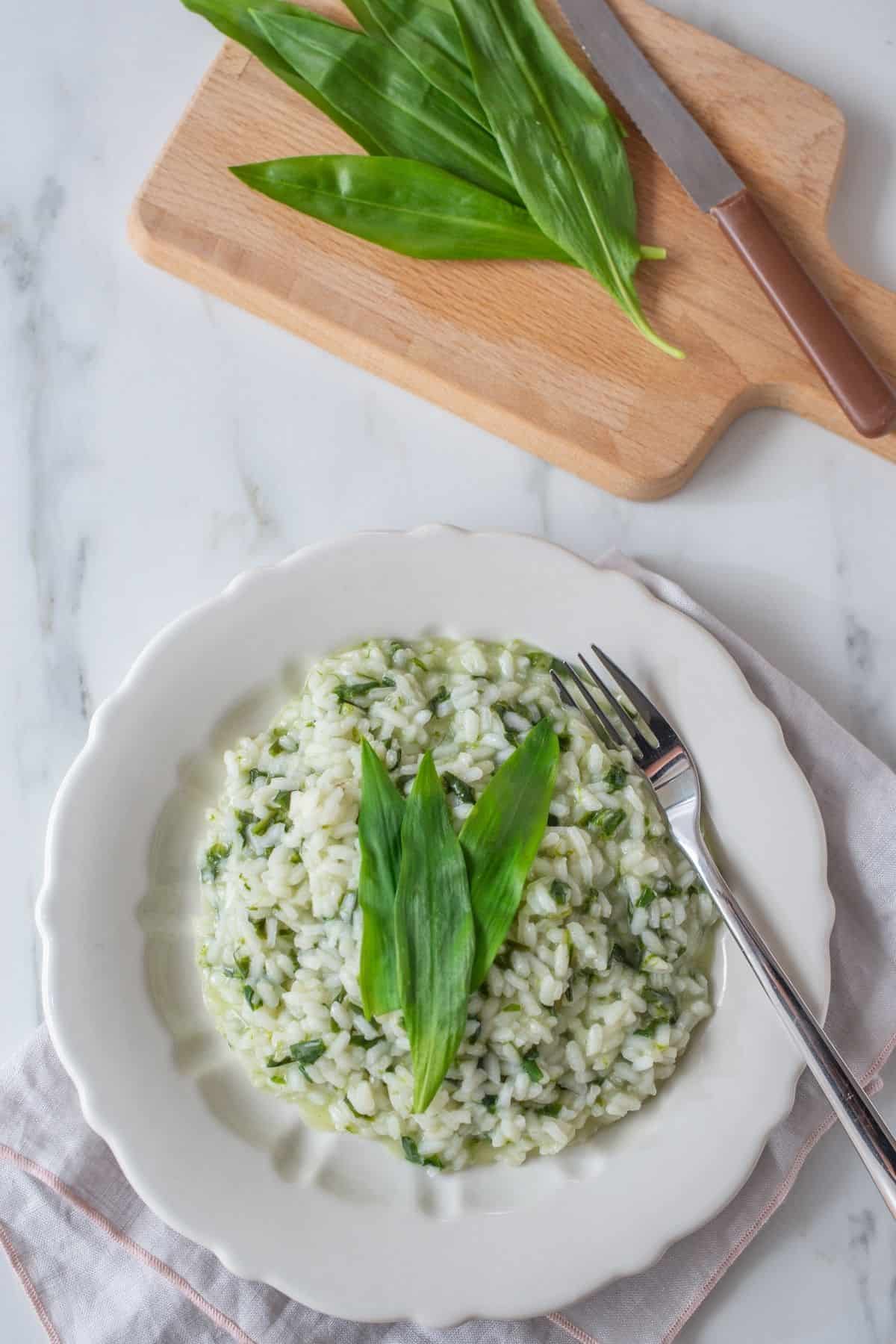 overhead shot of a plate with wild garlic risotto next to a cutting board with wild garlic leaves 