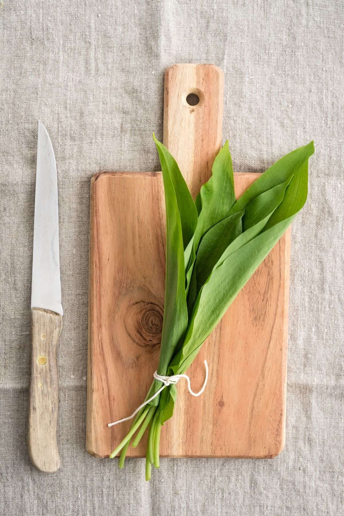 a cutting board with wild garlic leaves and a knife