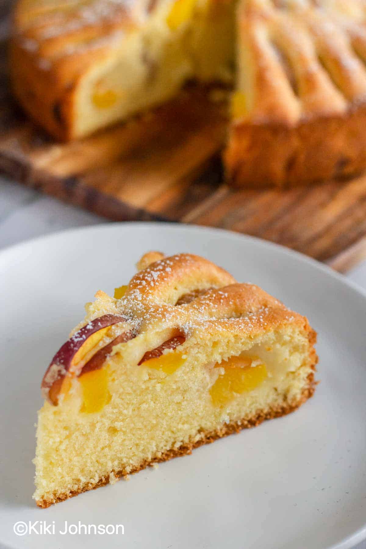 a slice of German peach cake with fresh peach slices on a cake plate