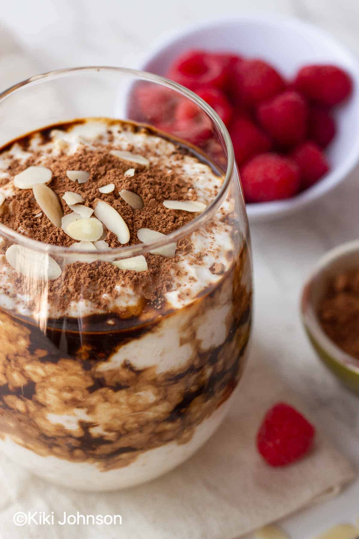 a glass with healthy vegan tiramisu overnight oats topped with cocoa powder and almonds 