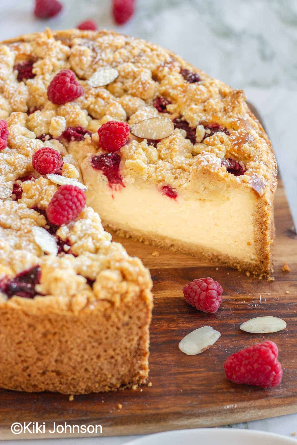 German Raspberry Crumble Cheesecake on a wooden board with one slice missing