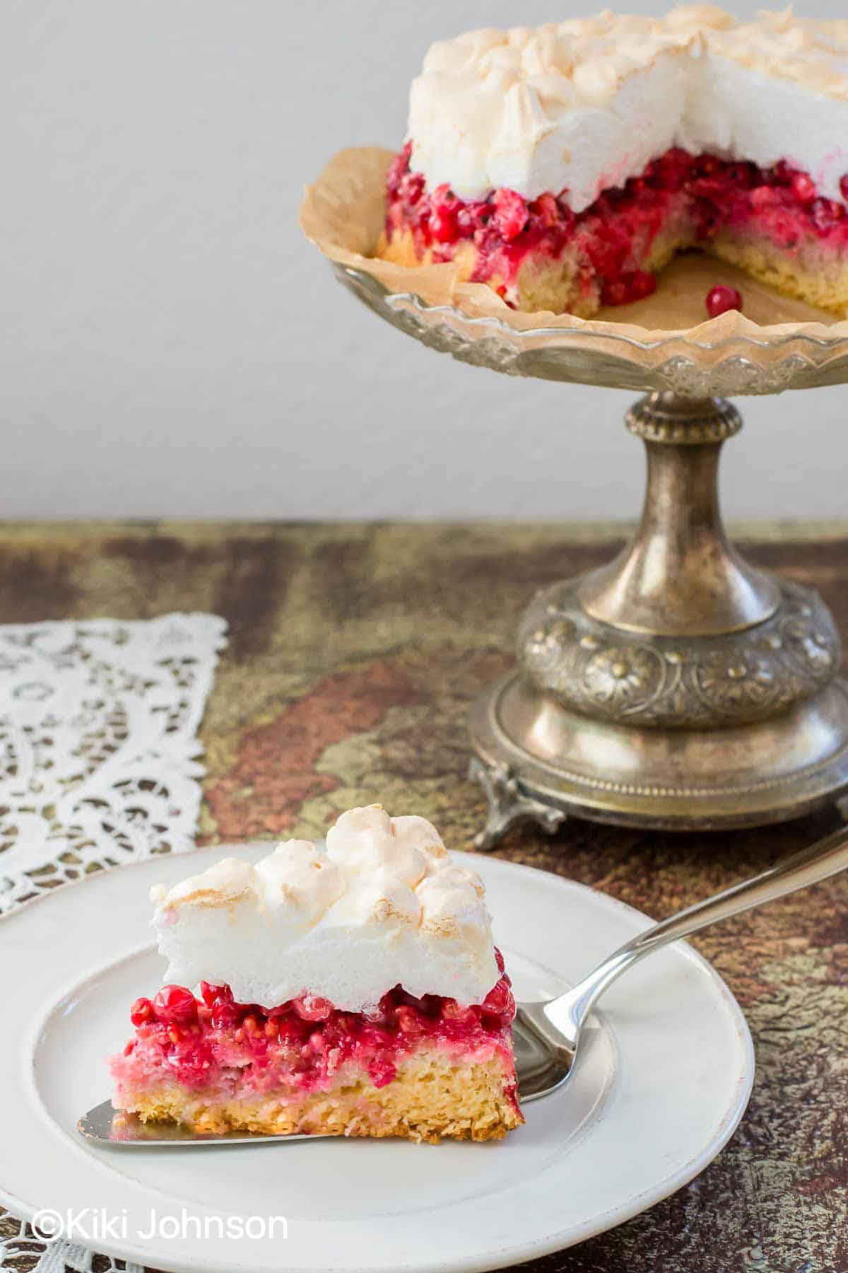 ein Stück Johannisbeerkuchen mit Baiser, roten Johannisbeeren und Rührteig auf einem Kuchenteller 