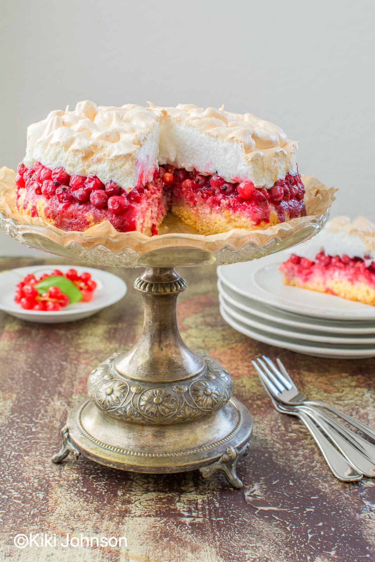 German fresh red currant meringue cake on a silver cake stand with one slice missing