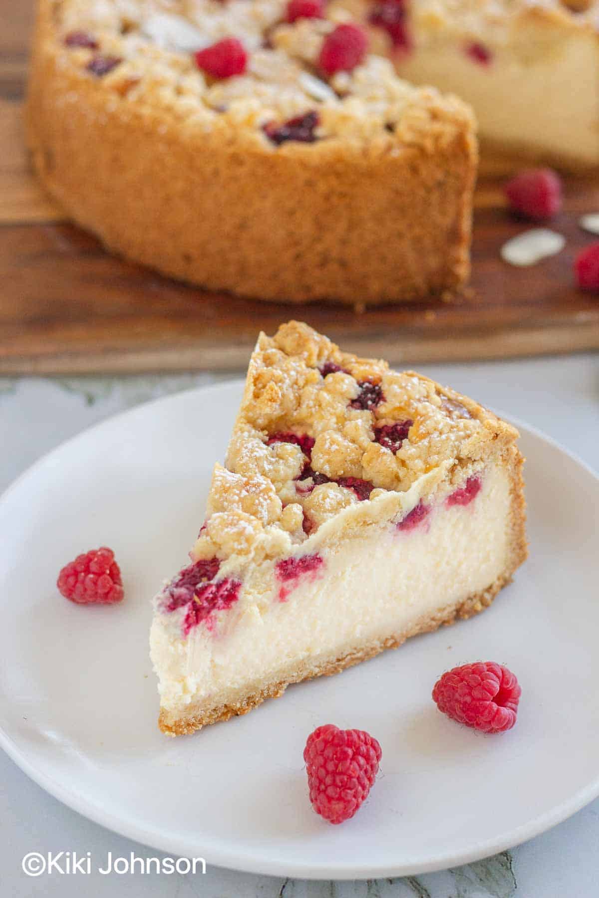 a slice of baked German Raspberry Crumble Cheesecake with Streusel on a plate with fresh raspberries 