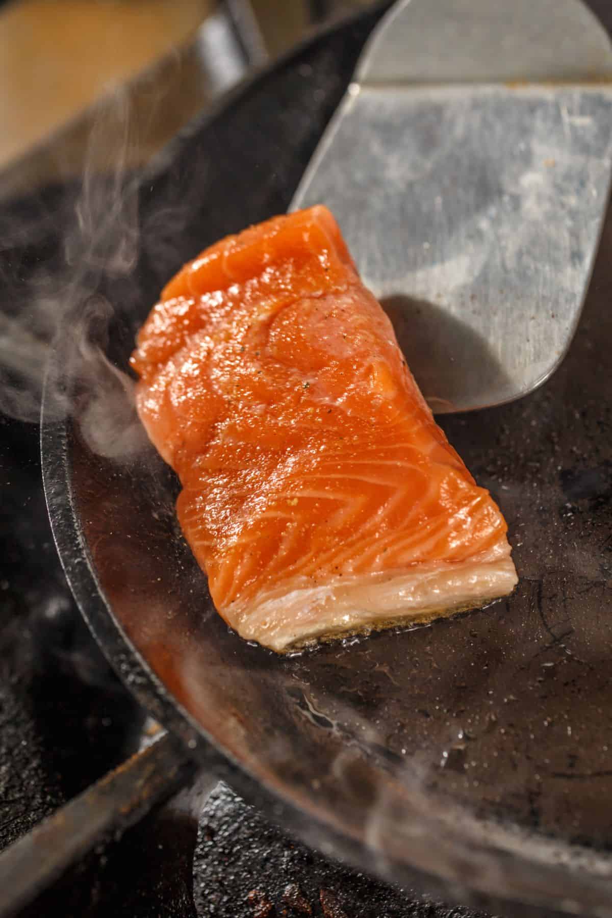 a salmon fillet being fried in a pan 