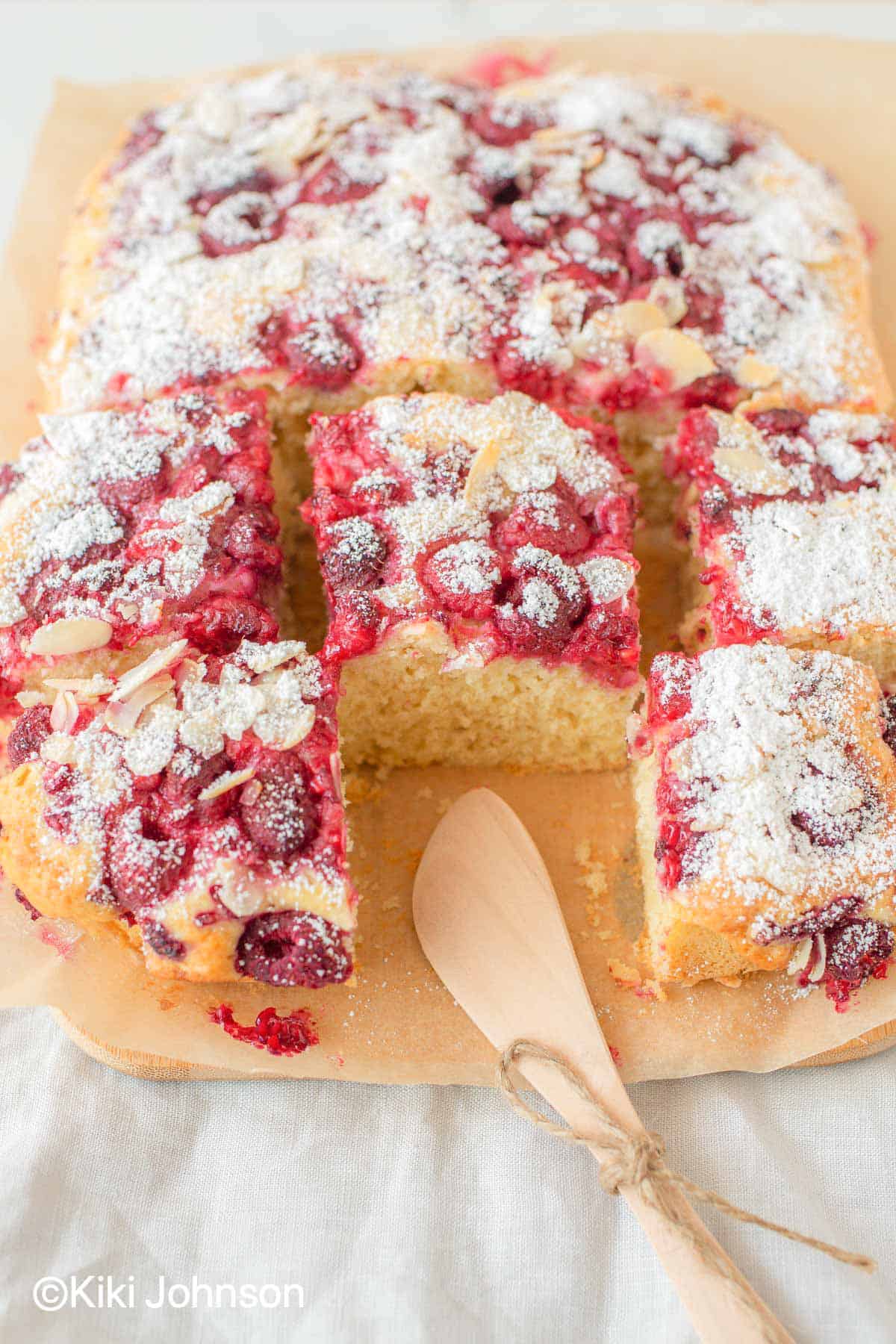 German Raspberry Cake topped with slivered almonds and icing sugar on a sheet of parchment