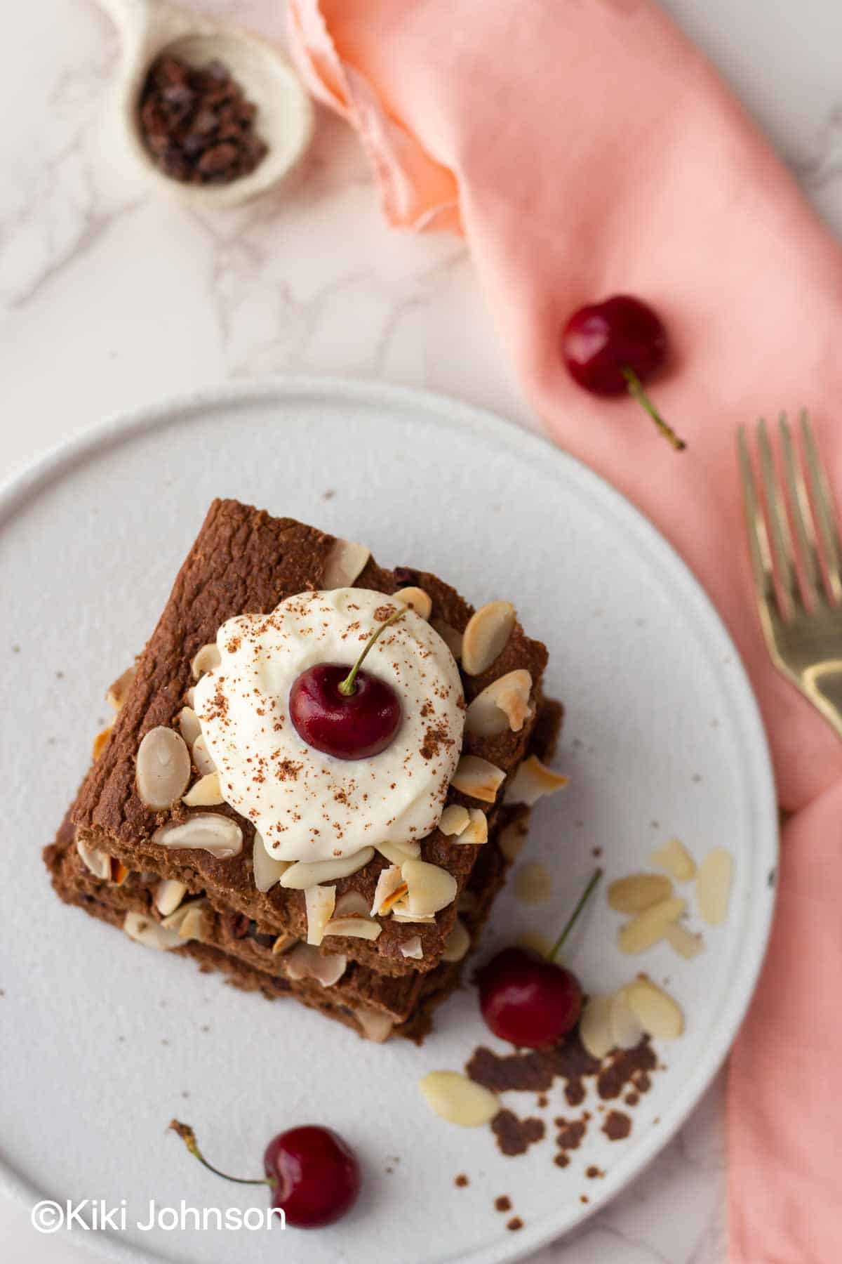 stacked glutenfree chocolate sheetpan pancakes with whipped cream and fresh cherries