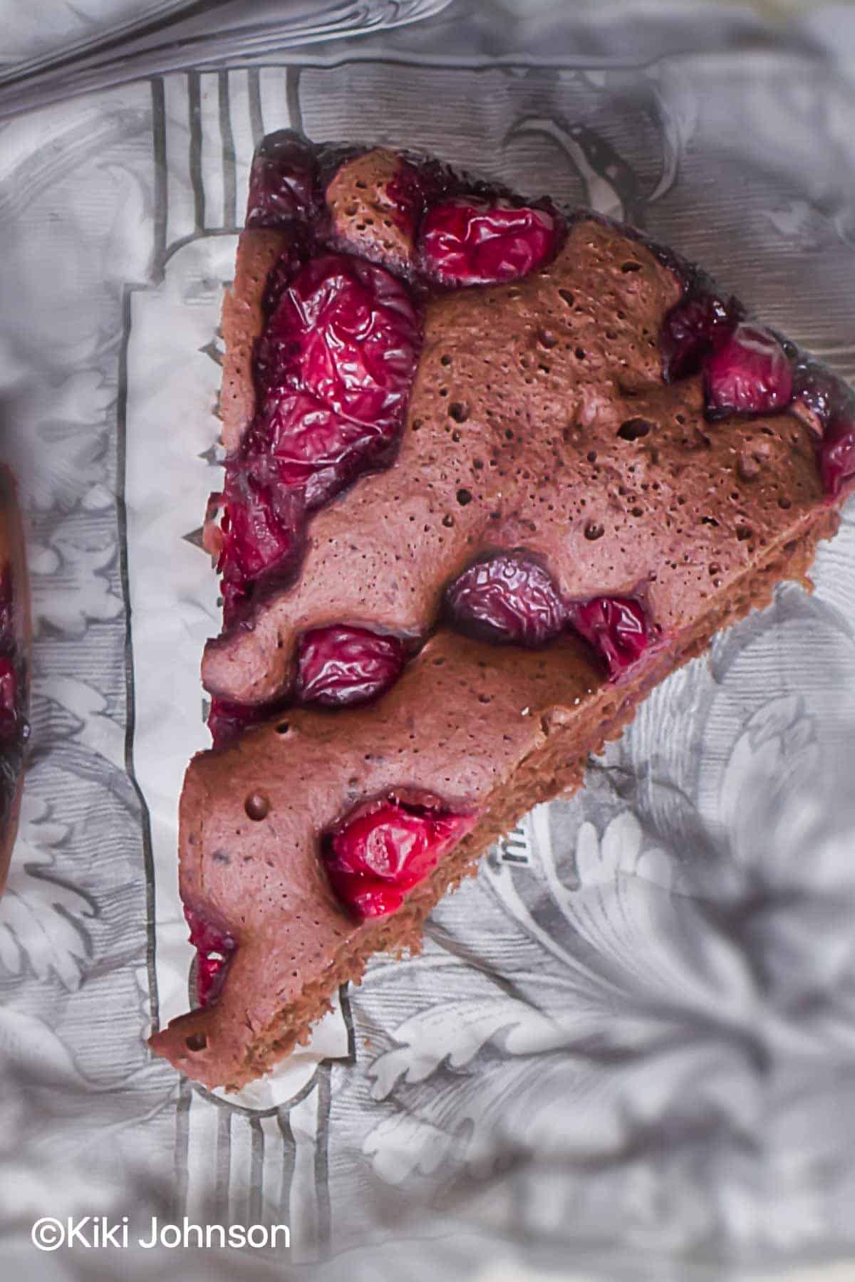 a slice of vegan cherry chocolate cake with fresh cherries on a silver plate.