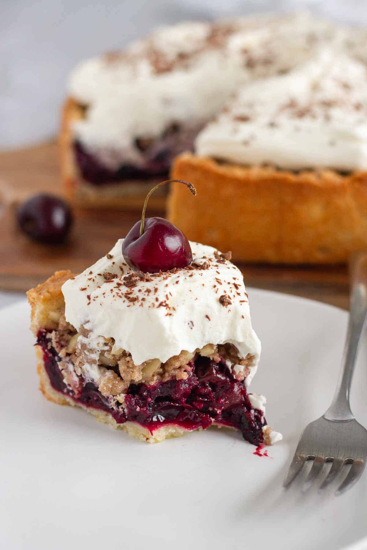 a half-eaten slice of German sour cherry cake topped with whipped cream and a fresh cherry 