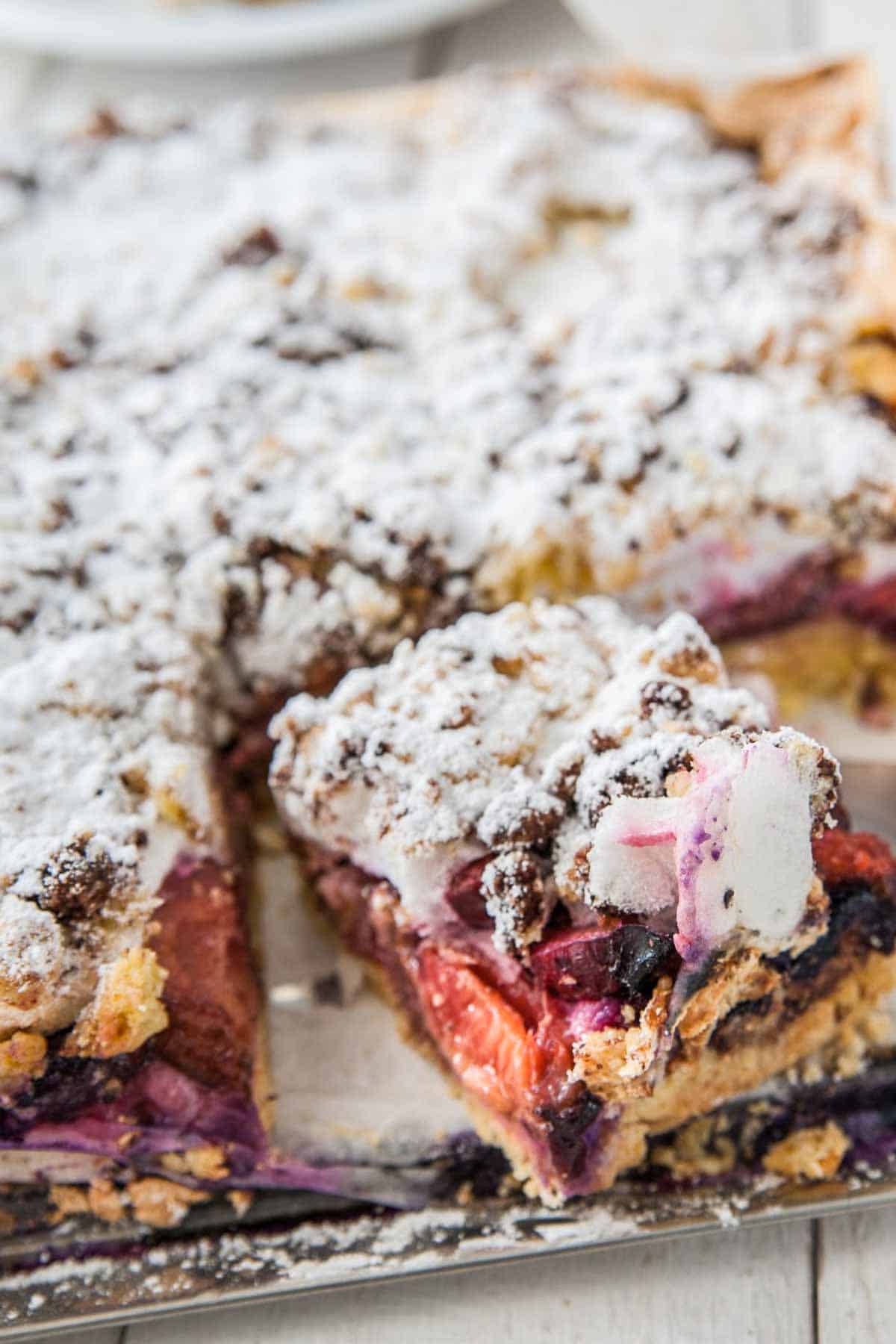 ein Stück Zwetschgen Kuchen mit Baiser und Streuseln wird von einem Kuchenblech genommen