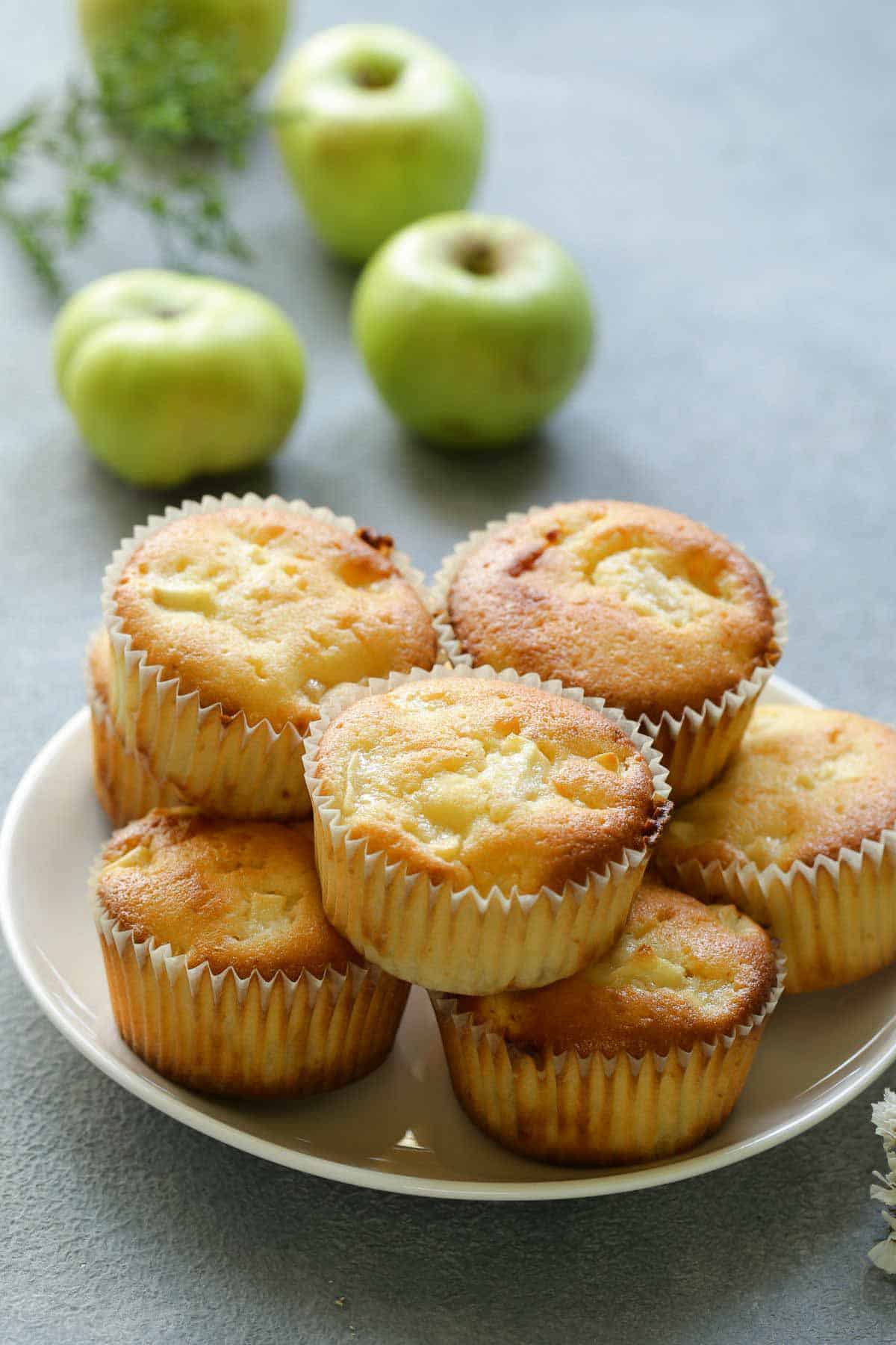 healthy thermomix apple muffins on a white plate with fresh apples in the background.
