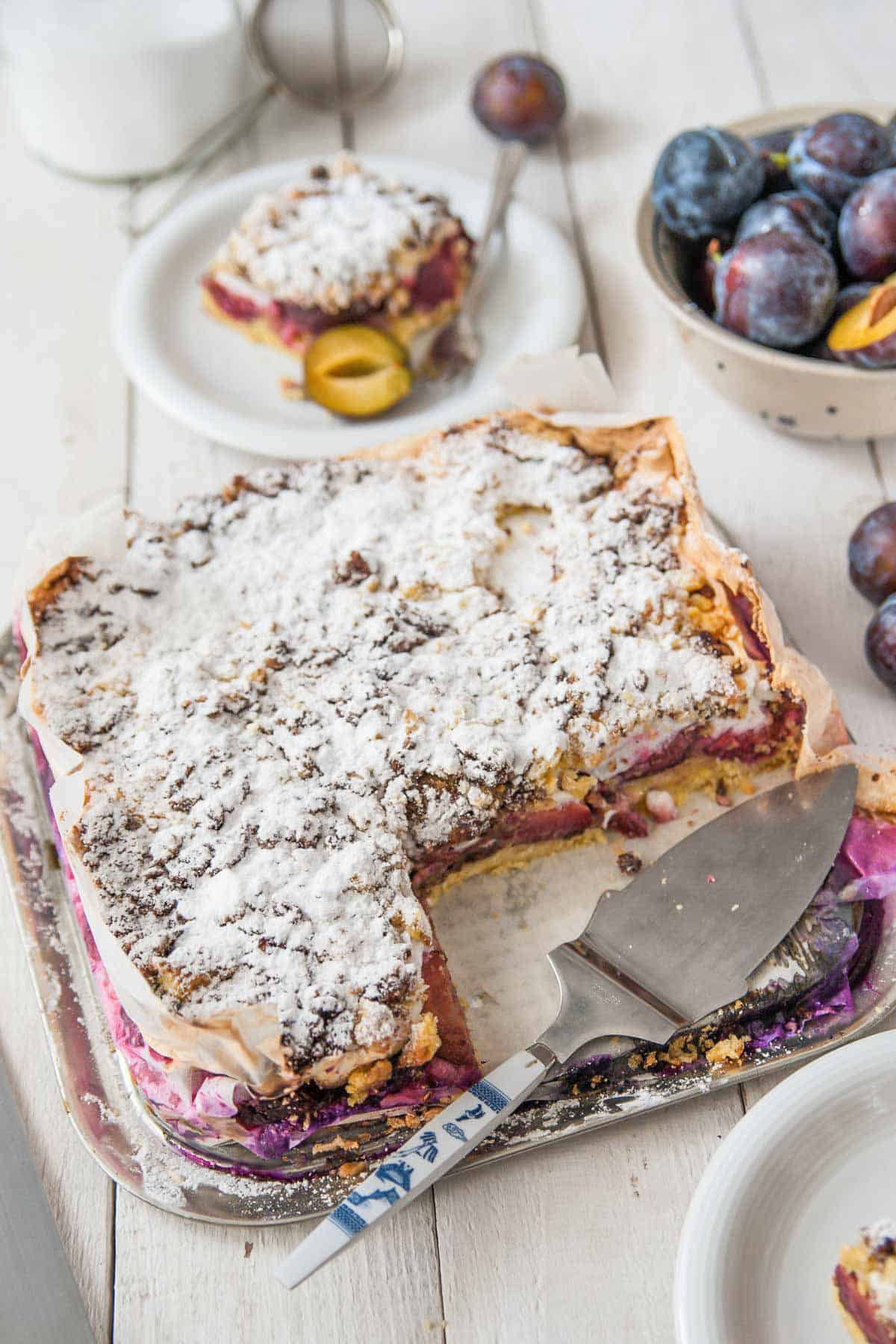 plum coffee cake with streusel topping and meringue on a sheetpan with a cake lifter and fresh prune plums on the side