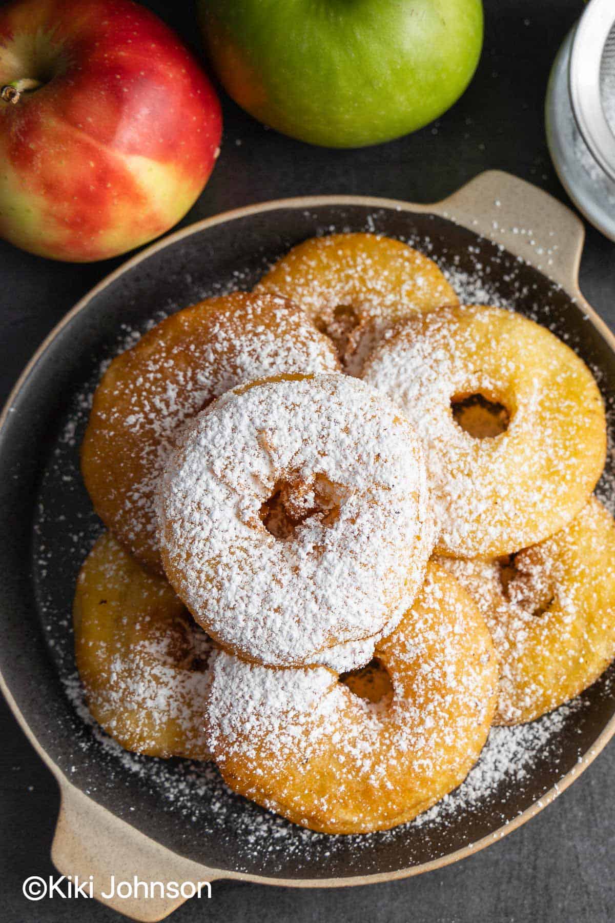 Old fashioned German apple fritters dusted with icing sugar on a black plate 